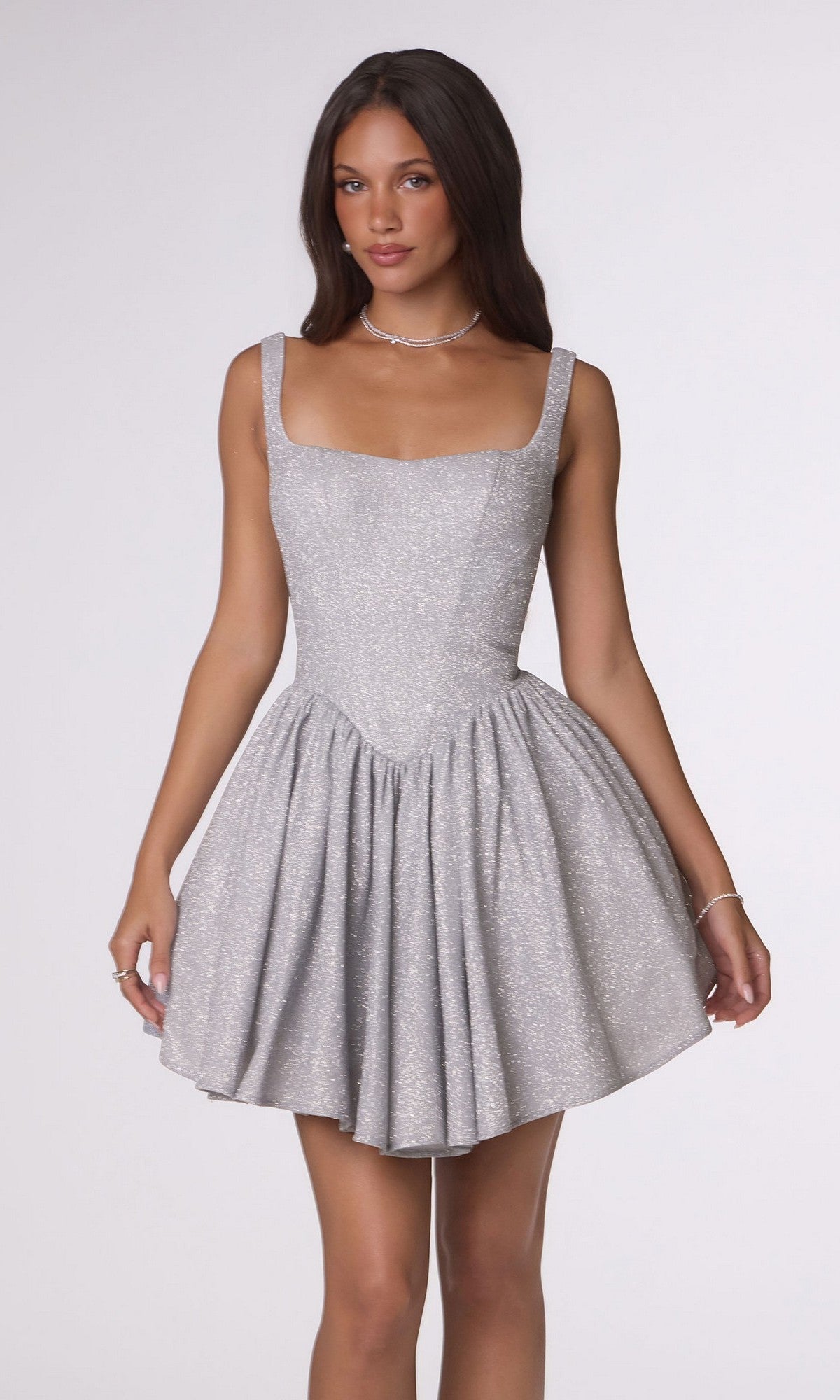 A woman stands against a plain light background wearing the Amoris T738 Short Homecoming Dress in silver, featuring a sleeveless design and a flared, short skirt.